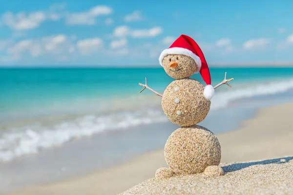 Sandstranden snögubbe i santa hatt. Holiday koncept för nya år och ch — Stockfoto