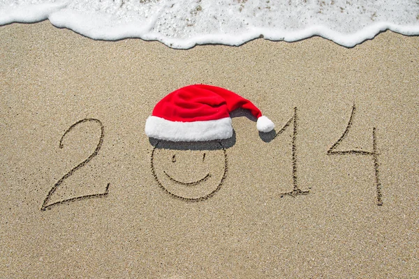 Szczęśliwego nowego roku 2014 z uśmiechniętą twarz w Boże Narodzenie kapelusz na piaszczystej b — Zdjęcie stockowe