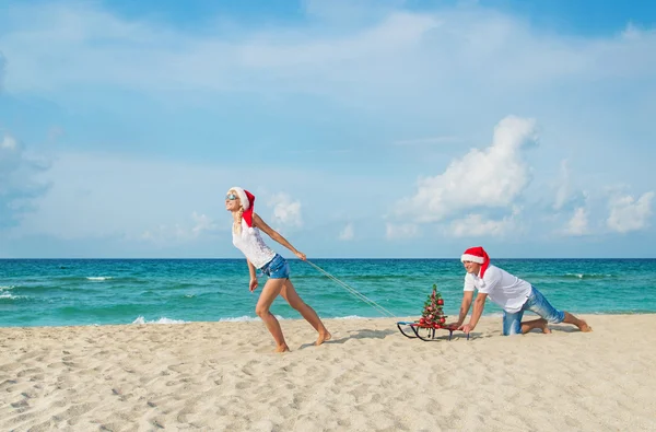 Młoda para działa na morzu plaży w santa kapelusze z sanki i ch — Zdjęcie stockowe