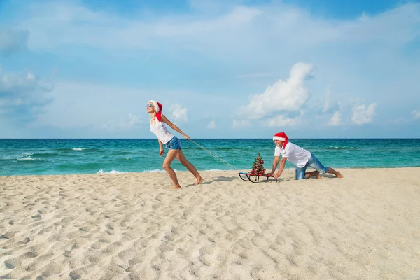 Genç bir çift deniz plaj santa şapkalar kızak ve ch ile çalışan — Stok fotoğraf