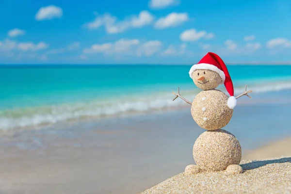 Pupazzo di neve sabbioso in cappello di Babbo Natale prendere il sole nel salone sulla spiaggia. Vacanza c — Foto Stock