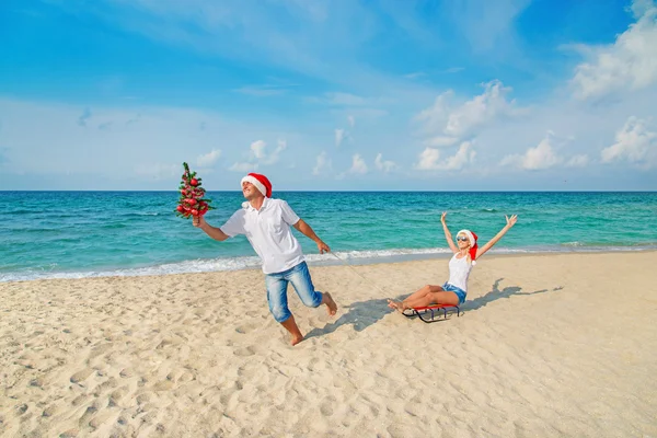若いカップルが海でサンタ帽子でビーチを実行します。 — ストック写真