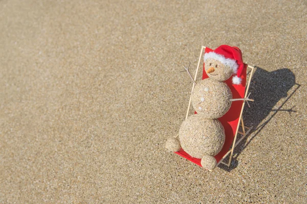 Sandy boneco de neve em santa chapéu banhos de sol no lounge de praia. Férias c — Fotografia de Stock