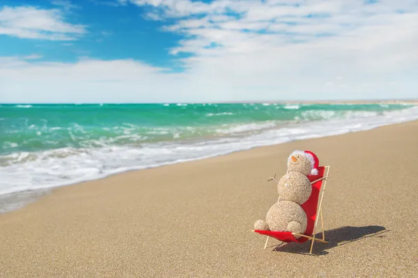 Sandschneemann mit Weihnachtsmütze sonnt sich in Strandlounge. Urlaub — Stockfoto