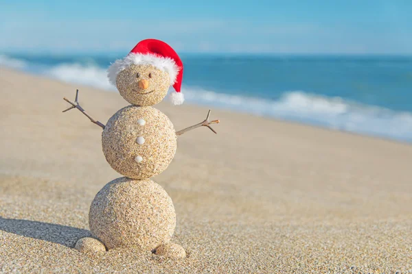 Um boneco de neve de areia sorridente no chapéu do Pai Natal. Conceito de férias de Ano Novo — Fotografia de Stock
