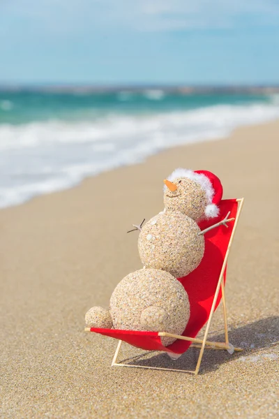 Αμμώδη χιονάνθρωπο σε santa καπέλο ηλιοθεραπεία στην παραλία σαλόνι. διακοπές c — Φωτογραφία Αρχείου