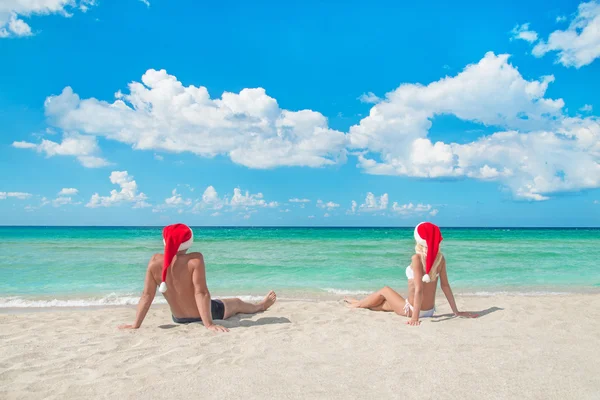 Lovers couple in santa hats at tropical sandy beach — Stock Photo, Image