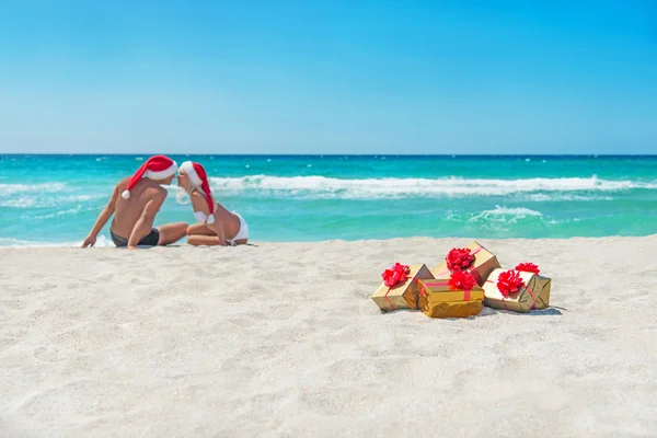 Całowanie miłośników para w santa kapelusze na morzu plaży — Zdjęcie stockowe