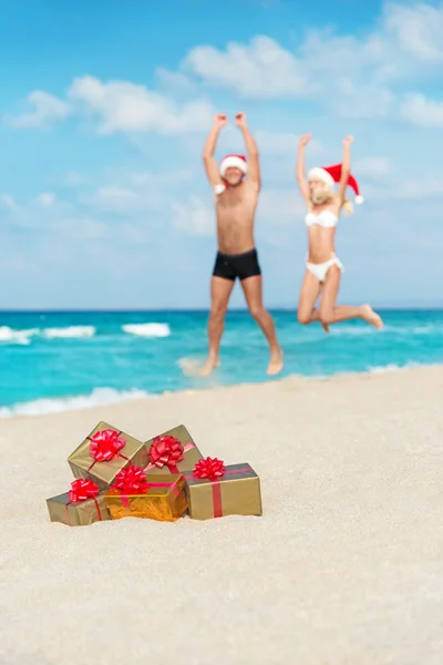 Felices amantes pareja en sombreros de santa saltar en la playa del mar — Foto de Stock