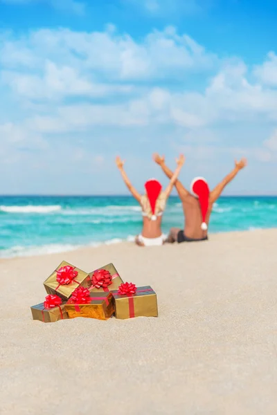 Happy couple in santa hats hands up at sea beach — Stock Photo, Image