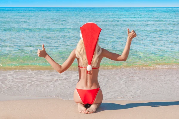 Deniz sahilinde kırmızı Noel şapkalı güzel sarışın kadın. — Stok fotoğraf
