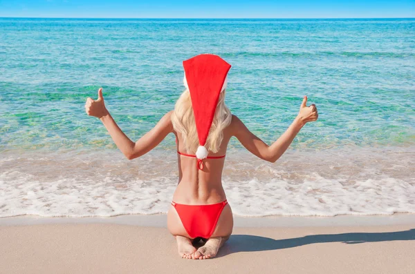 Beautiful blonde woman in red christmas hat on sea beach. — Stock Photo, Image