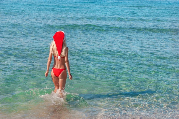Belle femme blonde en chapeau de Noël rouge sur la plage de la mer . — Photo