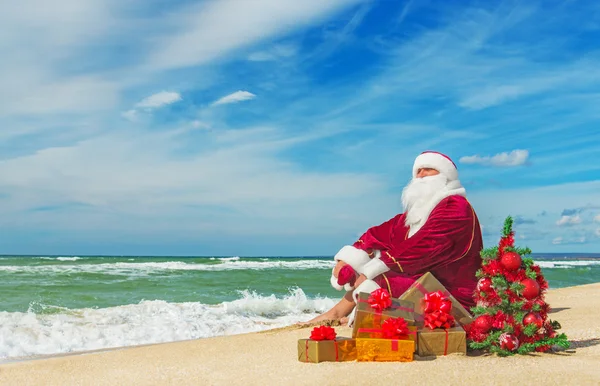 Papai Noel na praia do mar com muitos presentes — Fotografia de Stock