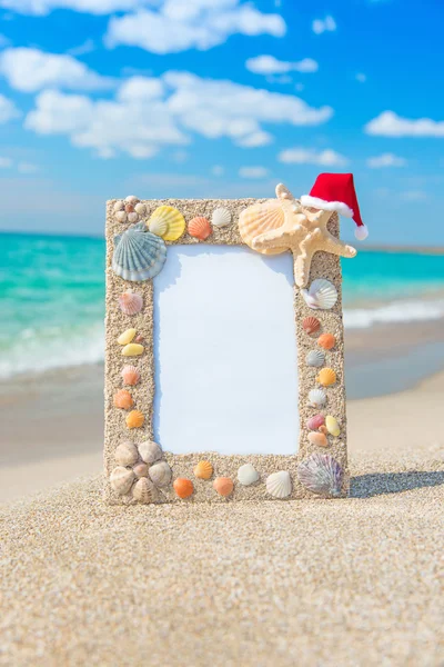 Sea shells frame with christmas hat against sea beach — Stock Photo, Image