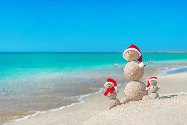 Schneemänner Familie am Meeresstrand mit Weihnachtsmütze. — Stockfoto