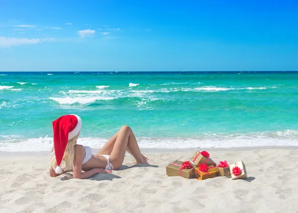 Mooie blonde vrouw in bikini, rode kerst hoed en geschenk doos — Stockfoto