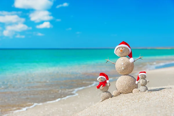 Snowmans rodina na mořské pláži v santa hat. — Stock fotografie