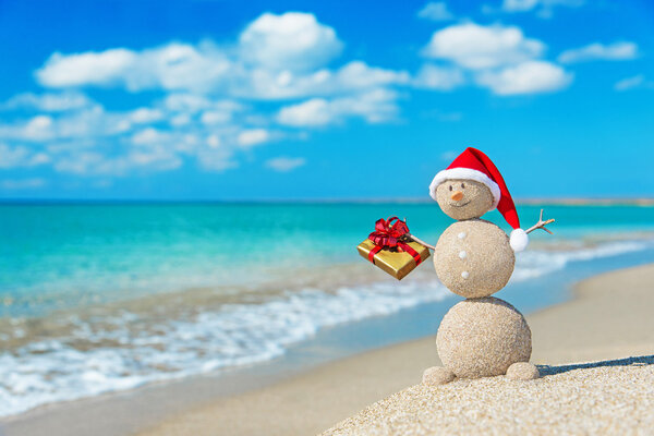 Smiley sandy snowman at beach in christmas hat