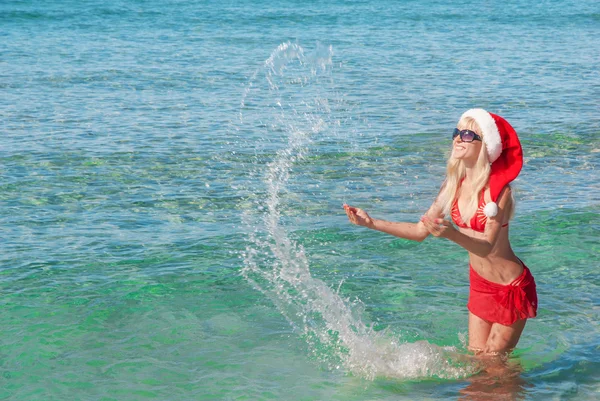 Hermosa mujer rubia en sombrero de navidad rojo en la playa del mar —  Fotos de Stock