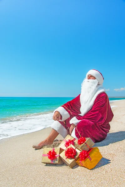 Санта-Клаус с золотыми подарками отдыхает на морском пляже — стоковое фото