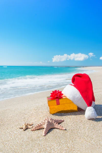 Santa claus klobouk a Vánoční dárková krabička na pobřeží — Stock fotografie