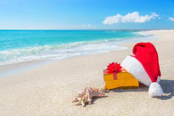 Шляпа Санта-Клауса и рождественская подарочная коробка на берегу моря с морем — стоковое фото