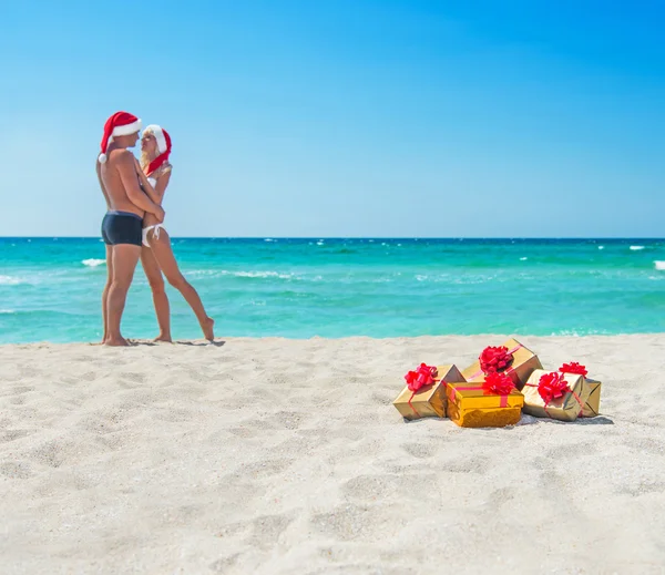 Całowanie miłośników para w santa kapelusze na morzu plaży — Zdjęcie stockowe