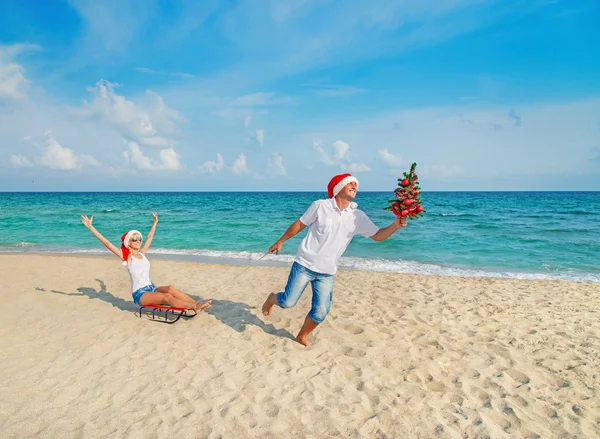 Young couple running at sea beach in santa hats — Stock Photo, Image