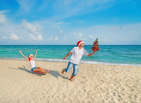 Pareja joven corriendo en la playa de mar en sombreros de santa —  Fotos de Stock