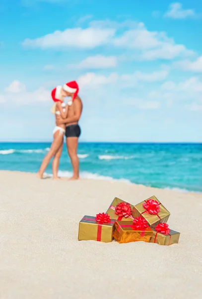 Besos pareja en sombreros de santa en la playa de mar con —  Fotos de Stock