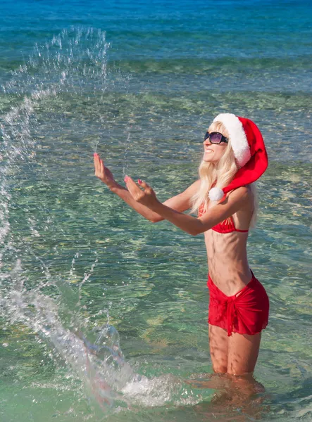 Hermosa mujer rubia en sombrero de navidad rojo en la playa del mar —  Fotos de Stock