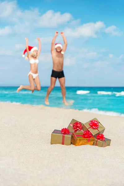 Felices amantes pareja en sombreros de santa saltar en la playa del mar —  Fotos de Stock