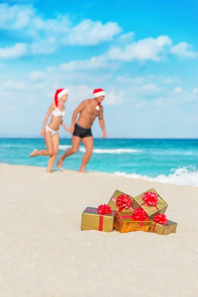 Running couple in santa hats at sea beach — Stock Photo, Image