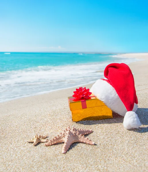 Chapéu de Papai Noel e caixa de presente de Natal na praia — Fotografia de Stock