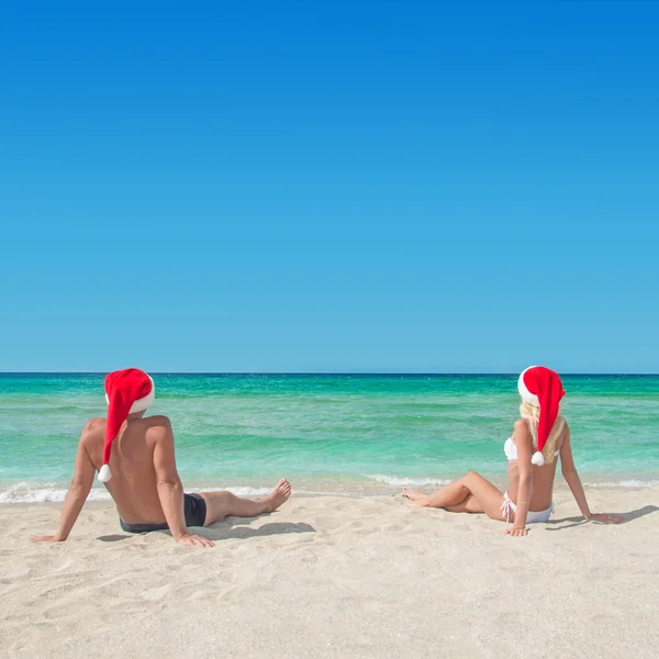 Los amantes de la pareja en sombreros de santa en la playa de arena tropical - Navidad —  Fotos de Stock