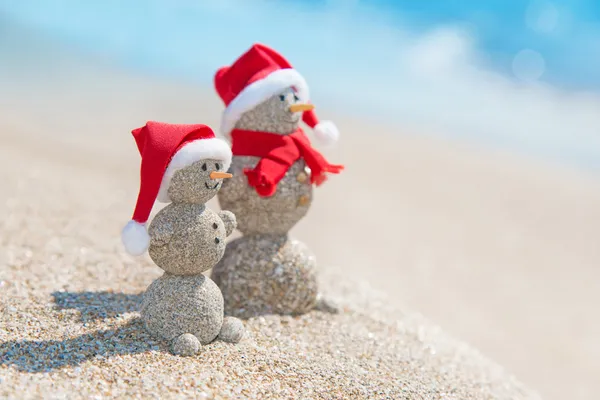 Snowmans 夫妇在海上沙滩圣诞帽子. 图库图片