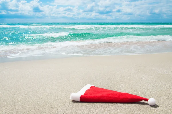 Chapéu de Papai Noel na praia contra ondas e céu azul — Fotografia de Stock