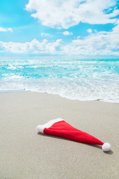 Jultomten hatt på havsstranden mot vågor och blå himmel — Stockfoto