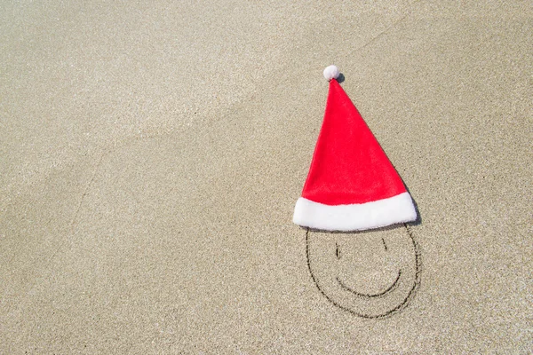 Santa Claus hat and smiley face on seashore against waves — Stock Photo, Image