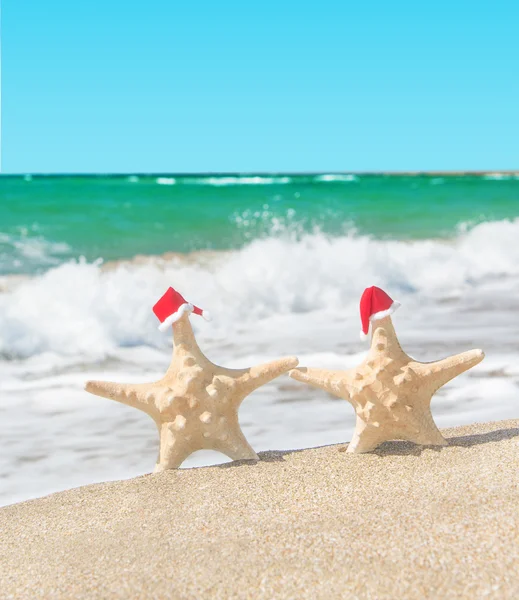 Sea-stars couple in santa hats walking at sea beach. — Stock Photo, Image