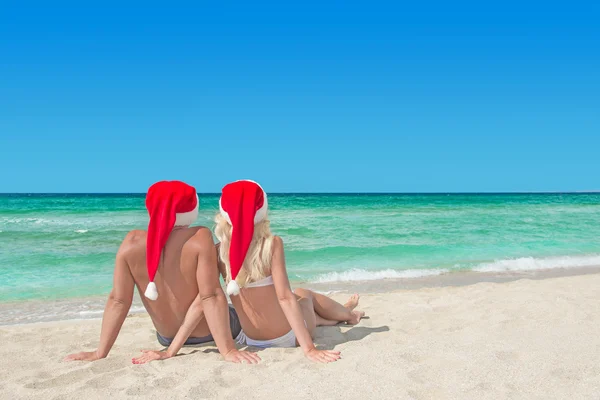 Lovers couple in red santa hats relaxing at tropical sandy beach — Stock Photo, Image
