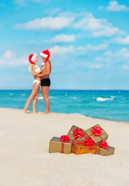 Hugging lovers couple in santa hats at sea beach with christmas — Stock Photo, Image