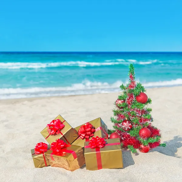 Árbol de Navidad y cajas de regalo de oro con gran lazo rojo en el mar — Foto de Stock