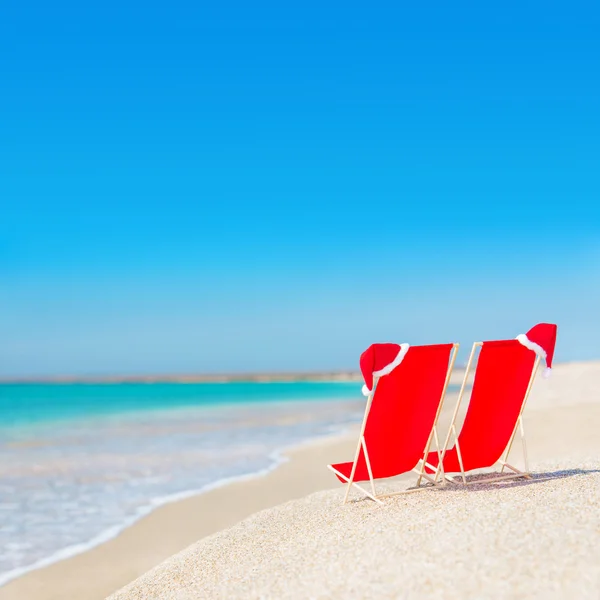 Kerstman hoed op chaise longues op wit zand strand tegen de zee — Stockfoto