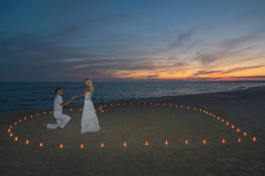 Couple in candles heart at sea beach sunset clipart