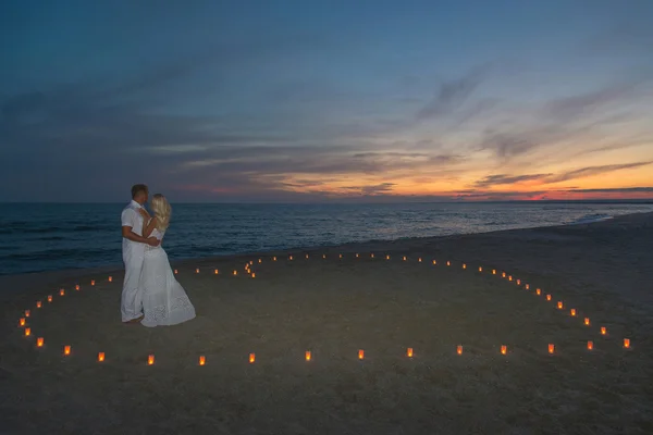 Jovem casal em velas coração no mar praia por do sol — Fotografia de Stock