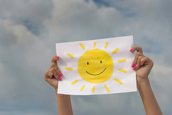 Sheet of paper with sun image against overcast sky