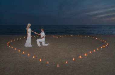Young couple in candles heart at sea beach against sunset clipart