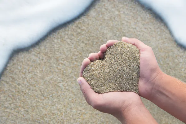 Mãos segurando uma areia na forma do coração - conceito de praia — Fotografia de Stock